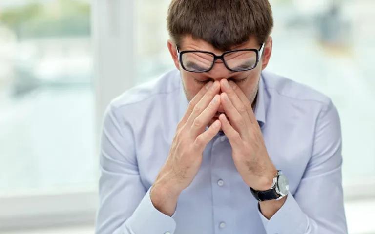 A man wearing glasses obscures his face with his hands.