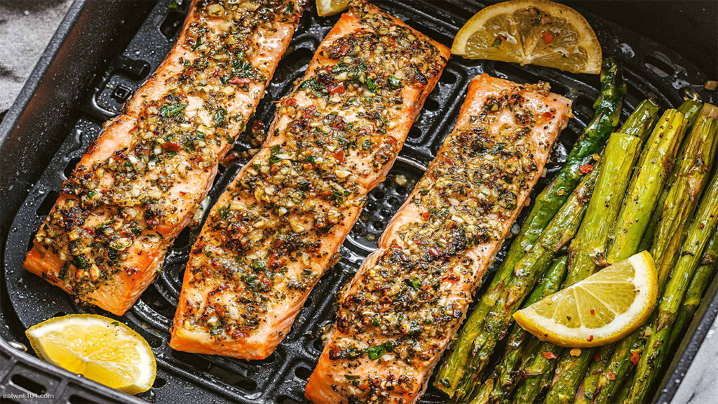 Herb-seasoned salmon with grilled asparagus and lemon wedges on a black grill pan.
