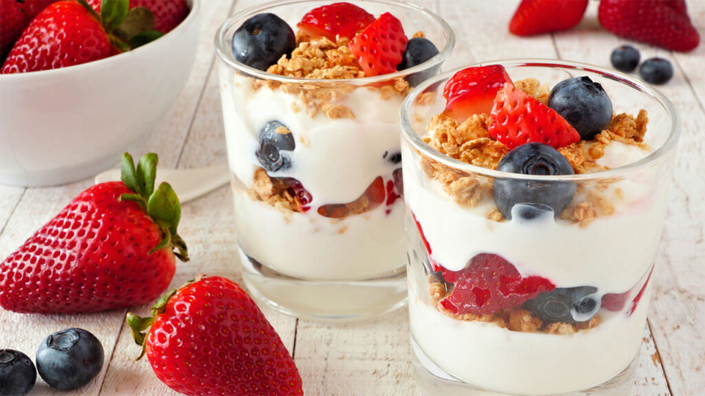 Layered yogurt parfait with granola, strawberries, blueberries, and fresh fruit in glass jars.