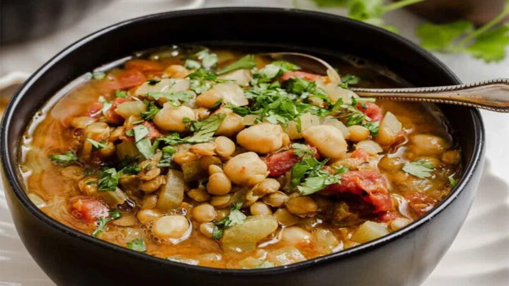 Lentil soup with tomatoes, carrots, cilantro, and protein-rich lentils in a black bowl.
