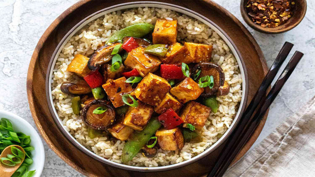 Tofu vegetable stir-fry over brown rice with bell peppers, mushrooms, and scallions