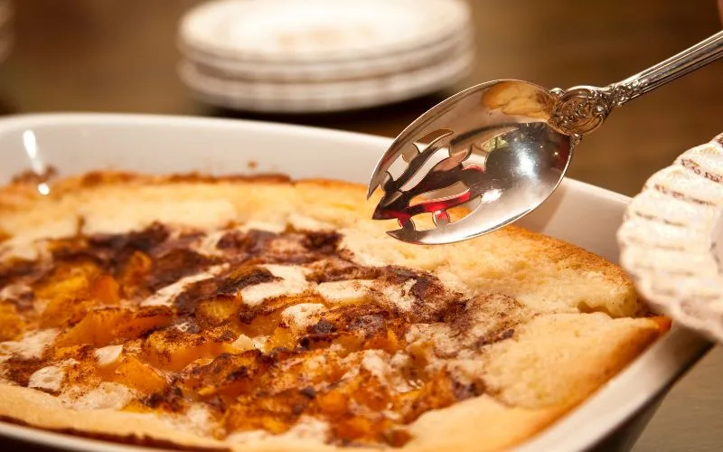 A hand holds a spoon, skillfully scooping food a dish.