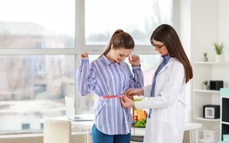 A healthcare professional assists a woman in measuring her waist.