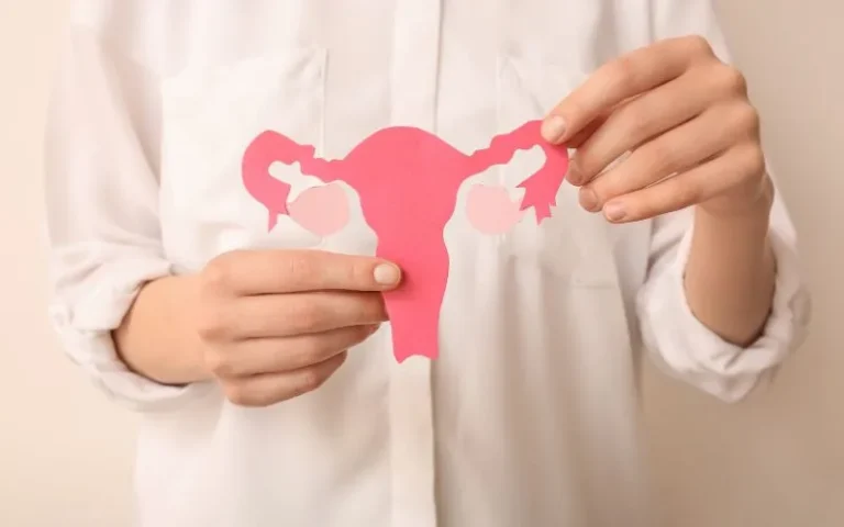 A woman proudly holds a pink paper cutout of a uterus.