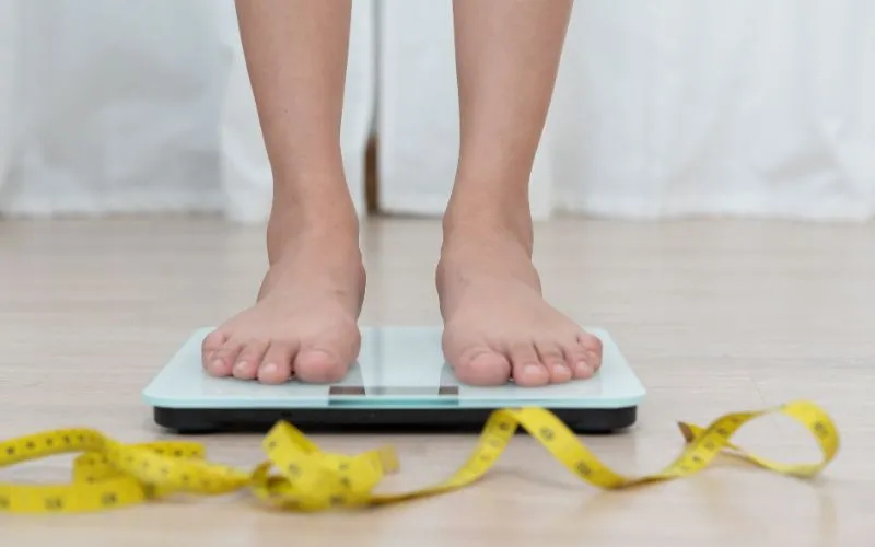 A woman measuring her weight with a yellow tape measur,