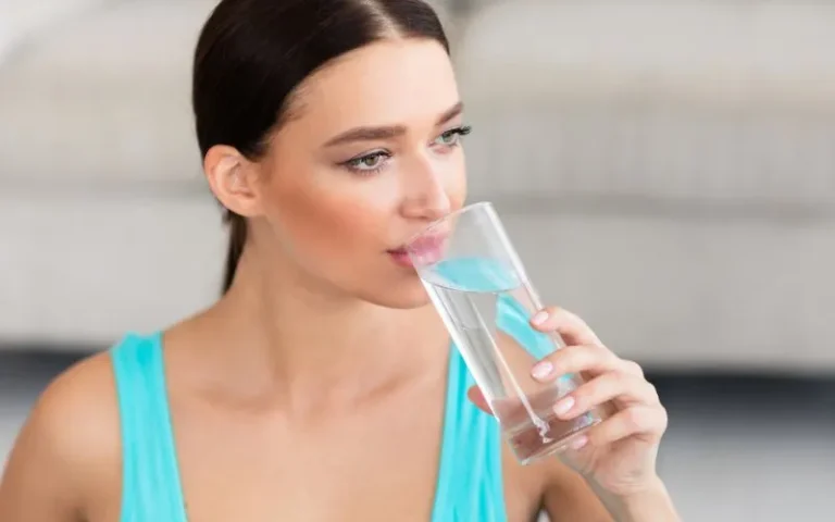 A woman enjoying a refreshing drink of water from a glass.