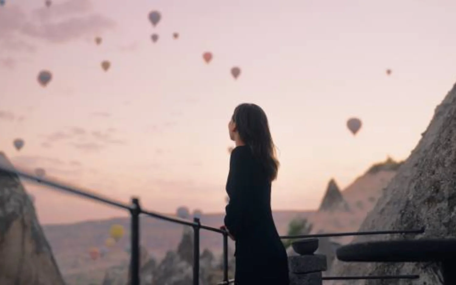 A woman in a black dress gazes at colorful hot air balloons.