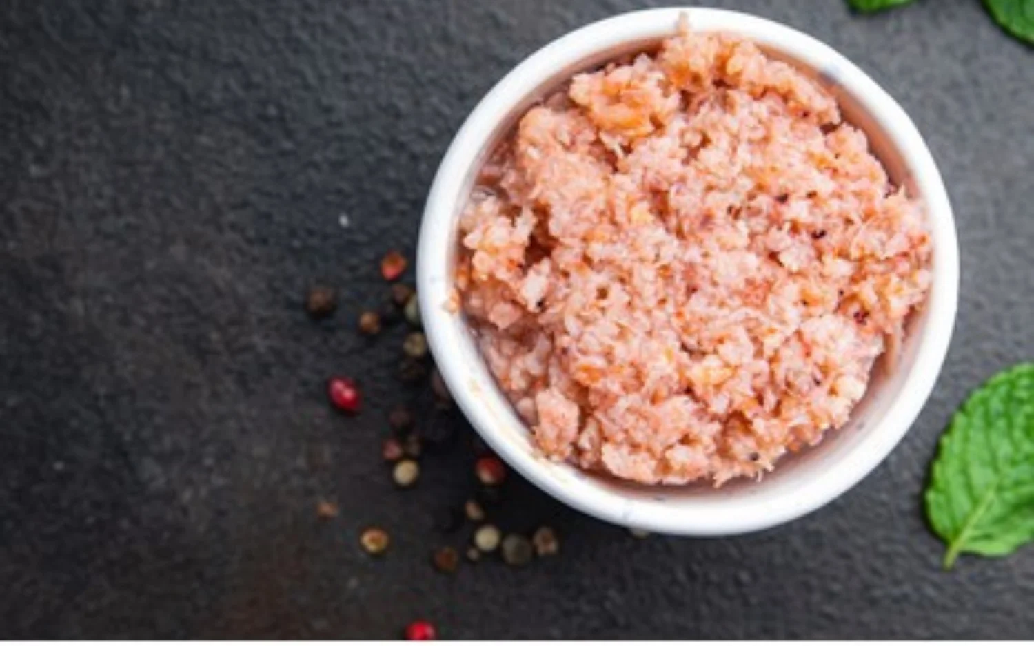 A bowl filled with pink salt, surrounded by an assortment of vibrant spices and fresh herbs, showcasing culinary diversity.