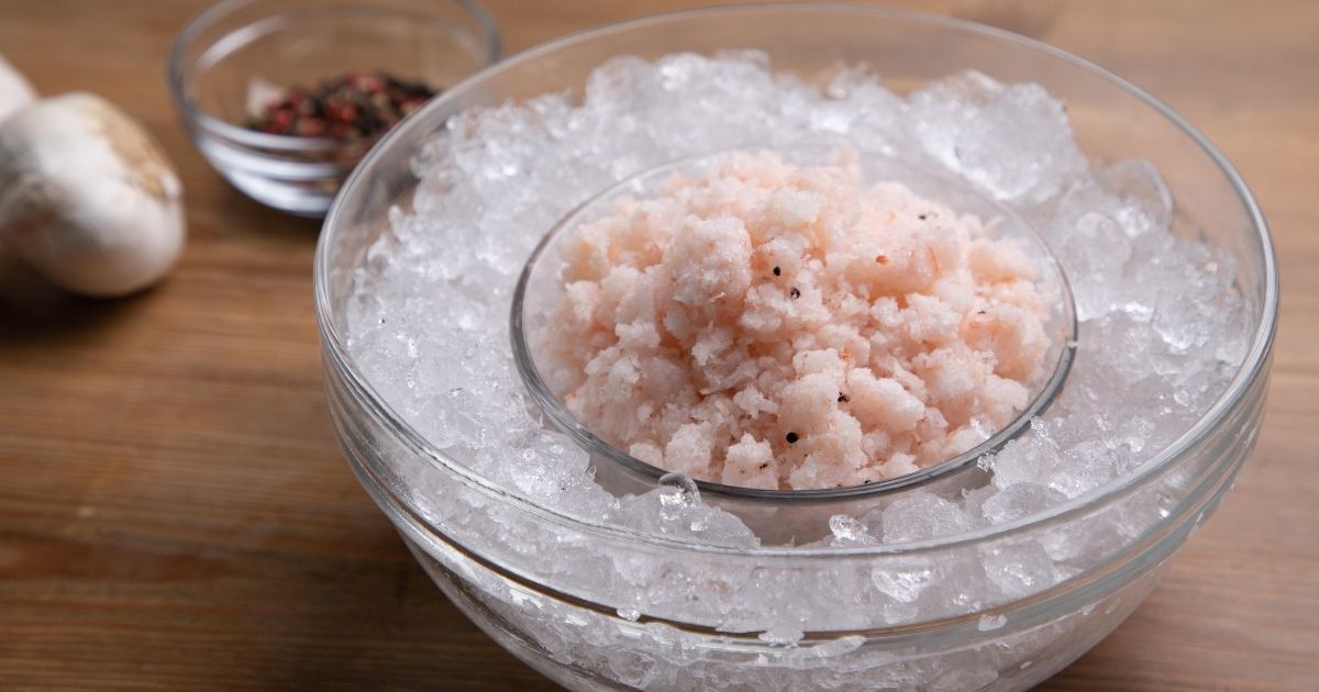 A bowl of finely chopped, raw crab meat surrounded by ice cubes,