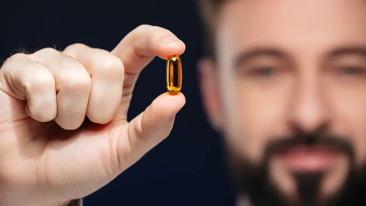 A bearded man holds a krill oil in his hand, contemplating