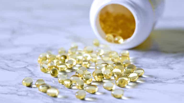 Fish Oil Nutrition: Tipped bottle spilling golden liquid capsules on marble surface.